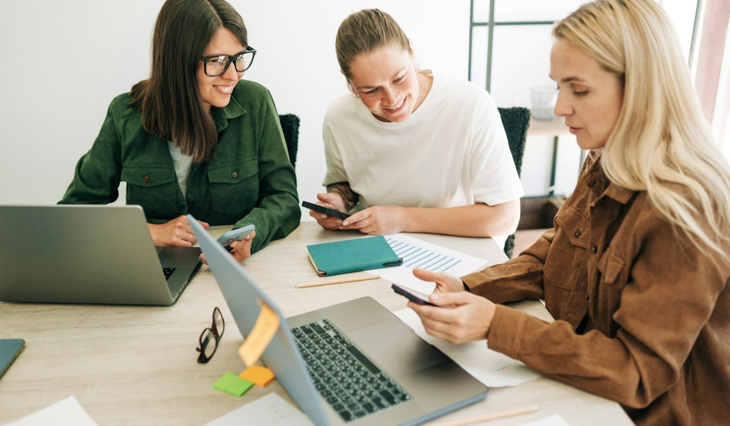 Female colleagues analyze social media marketing using mobile phone and laptops.